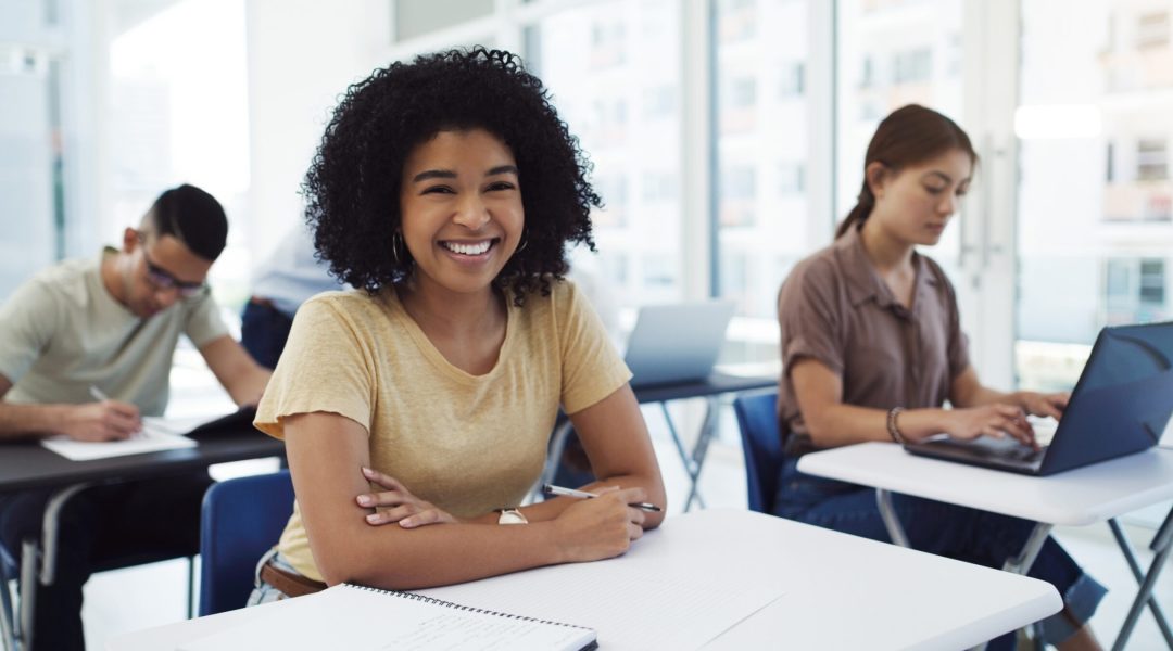 Portrait of a happy young student among her classmates in a classroom at university.