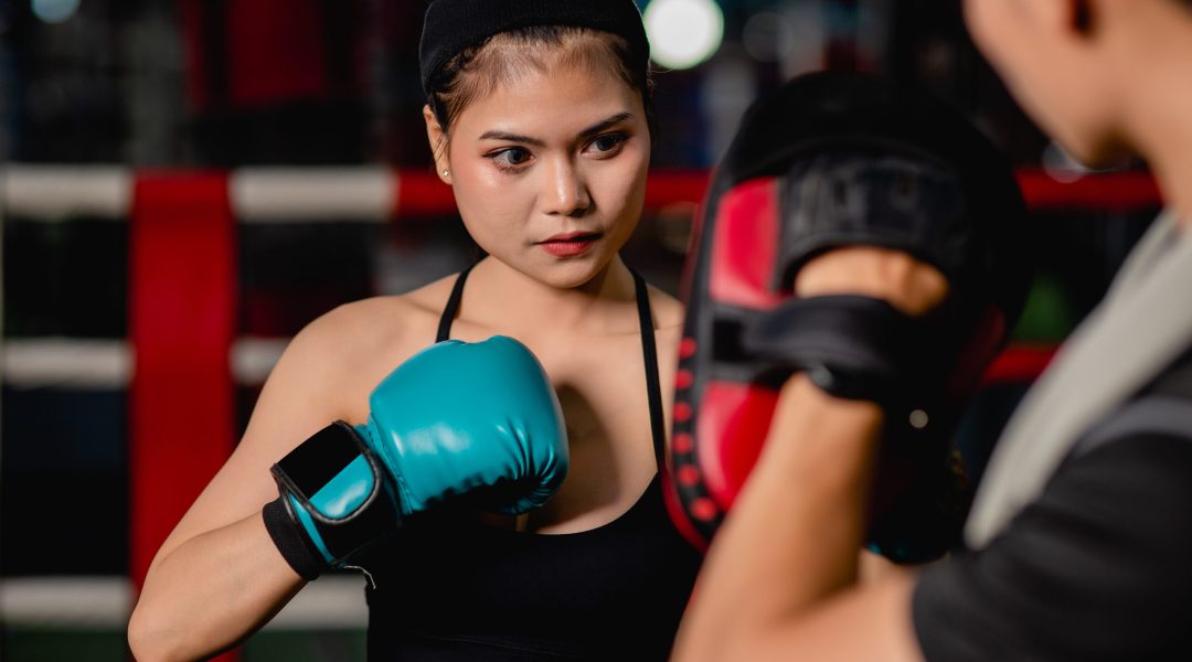 Close up portrait Young pretty woman exercising with handsome trainer at boxing and self defense class on the boxing ring at the gym, Female and male fight acting, selective focus and copy space