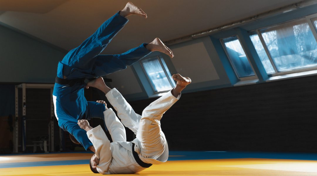 Two young fighters in kimono training martial arts in the gym. Concept of healthy lifestyle, sport, action, motion and movement. Two caucasian man practicing in white and blue kimono.